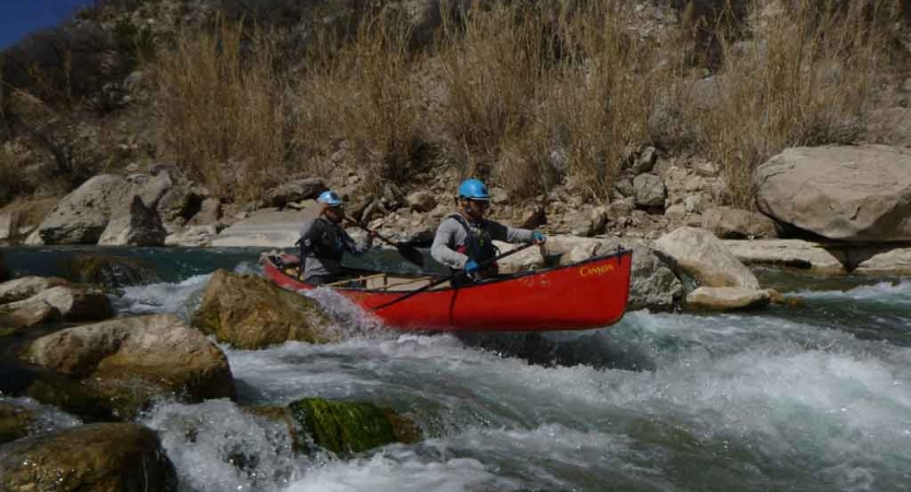 two gap year students paddle a canoe through whitewater on an outward bound expedition in texas